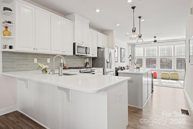 kitchen with sink, appliances with stainless steel finishes, white cabinetry, hanging light fixtures, and kitchen peninsula