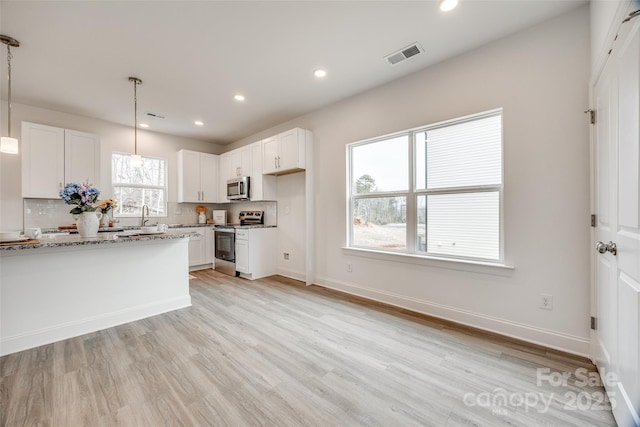 kitchen featuring light stone counters, appliances with stainless steel finishes, pendant lighting, light hardwood / wood-style floors, and white cabinets