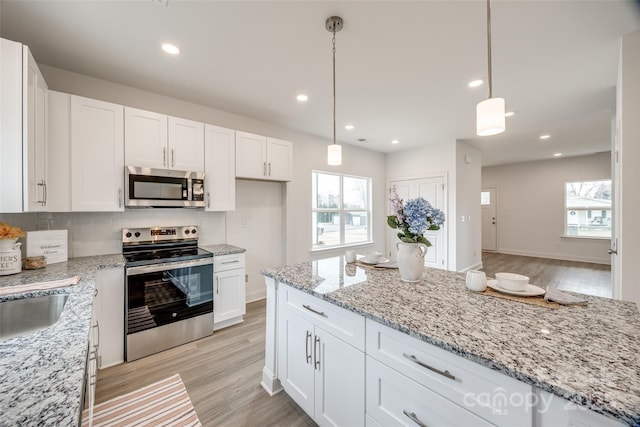 kitchen featuring decorative light fixtures, light hardwood / wood-style flooring, stainless steel appliances, light stone countertops, and white cabinets