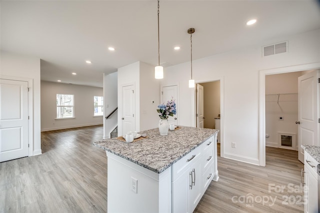 kitchen featuring a kitchen island, pendant lighting, white cabinetry, light stone countertops, and light hardwood / wood-style flooring