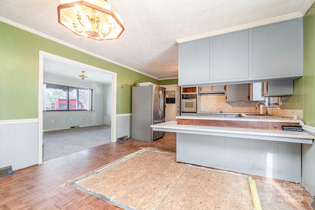 kitchen with appliances with stainless steel finishes, light countertops, a peninsula, and ornamental molding