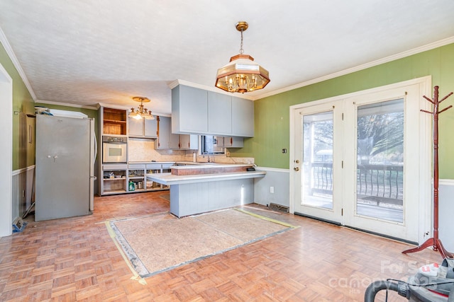 kitchen featuring a peninsula, freestanding refrigerator, light countertops, pendant lighting, and crown molding