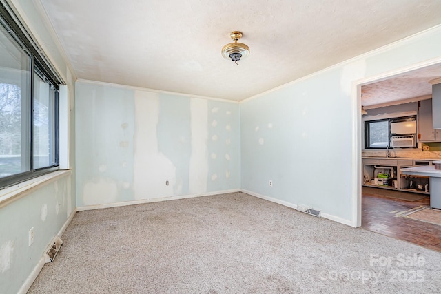 empty room with visible vents, carpet flooring, crown molding, and baseboards