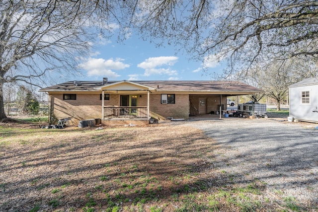 view of front of home featuring a porch, an attached carport, brick siding, and gravel driveway