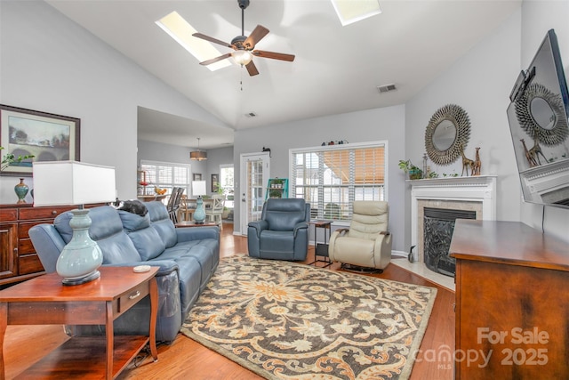 living room with lofted ceiling with skylight, light hardwood / wood-style floors, a premium fireplace, and ceiling fan