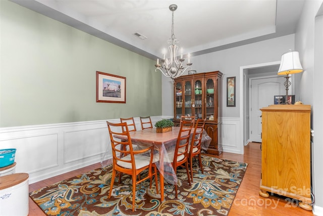 dining space with a raised ceiling, a chandelier, and light wood-type flooring