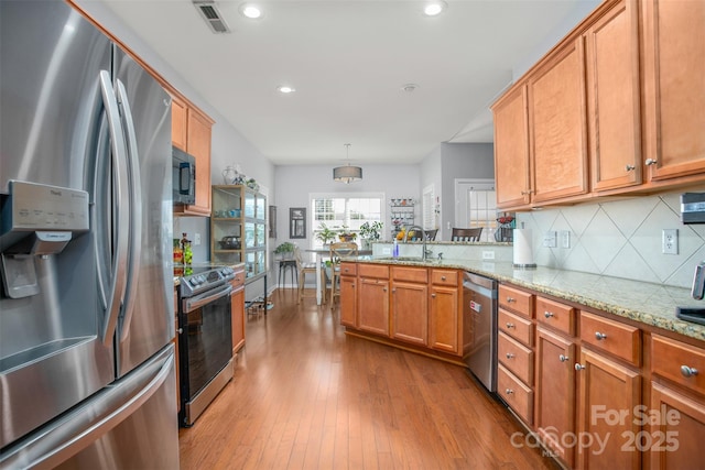 kitchen featuring hanging light fixtures, stainless steel appliances, light stone counters, kitchen peninsula, and light wood-type flooring