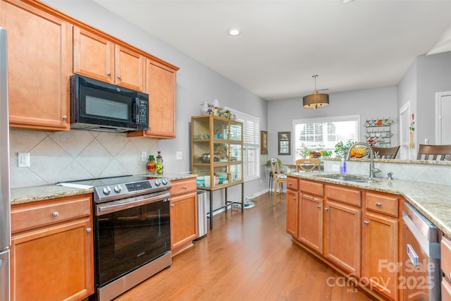 kitchen featuring sink, light wood-type flooring, pendant lighting, stainless steel appliances, and light stone countertops