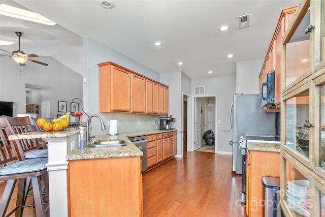 kitchen with sink, a breakfast bar area, kitchen peninsula, stainless steel appliances, and light stone countertops