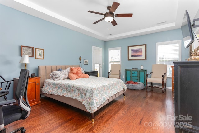 bedroom with a raised ceiling, dark hardwood / wood-style flooring, ceiling fan, and multiple windows