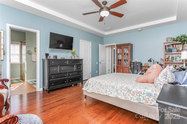 bedroom with a tray ceiling, wood-type flooring, and ceiling fan