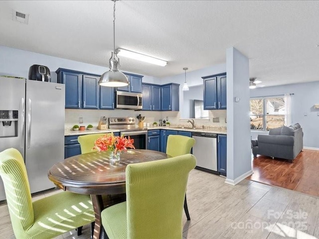 kitchen featuring sink, light hardwood / wood-style flooring, stainless steel appliances, blue cabinets, and decorative light fixtures