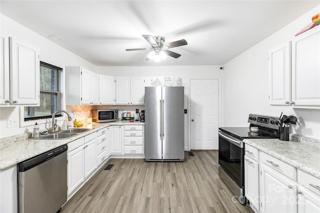 kitchen with appliances with stainless steel finishes, white cabinetry, sink, ceiling fan, and light hardwood / wood-style flooring