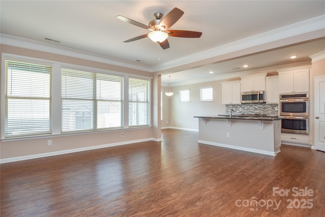 kitchen featuring a breakfast bar, white cabinetry, decorative backsplash, ornamental molding, and stainless steel appliances