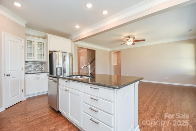 kitchen with sink, appliances with stainless steel finishes, dark stone countertops, white cabinets, and a center island with sink