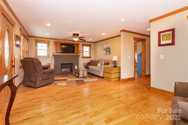 living room featuring crown molding, ceiling fan, a brick fireplace, and light wood-type flooring