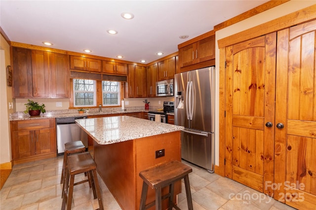 kitchen featuring sink, light stone counters, a center island, appliances with stainless steel finishes, and a kitchen breakfast bar