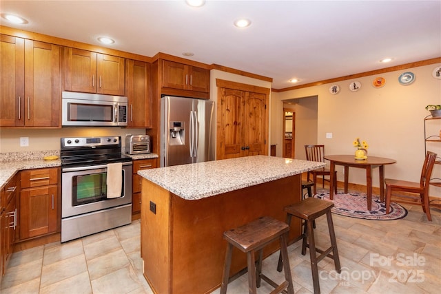 kitchen with appliances with stainless steel finishes, a center island, light stone counters, ornamental molding, and a kitchen bar