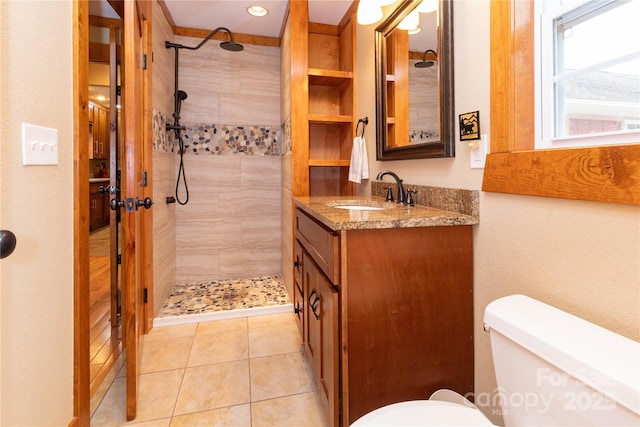 bathroom with tile patterned flooring, vanity, tiled shower, and toilet