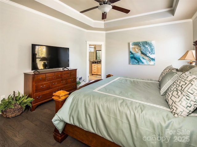 bedroom with crown molding, dark wood-type flooring, ceiling fan, connected bathroom, and a tray ceiling