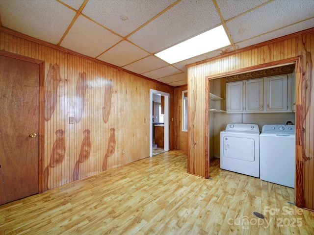 clothes washing area featuring separate washer and dryer, light hardwood / wood-style flooring, cabinets, and wooden walls