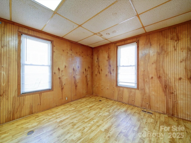 empty room featuring a drop ceiling, wood-type flooring, and wood walls