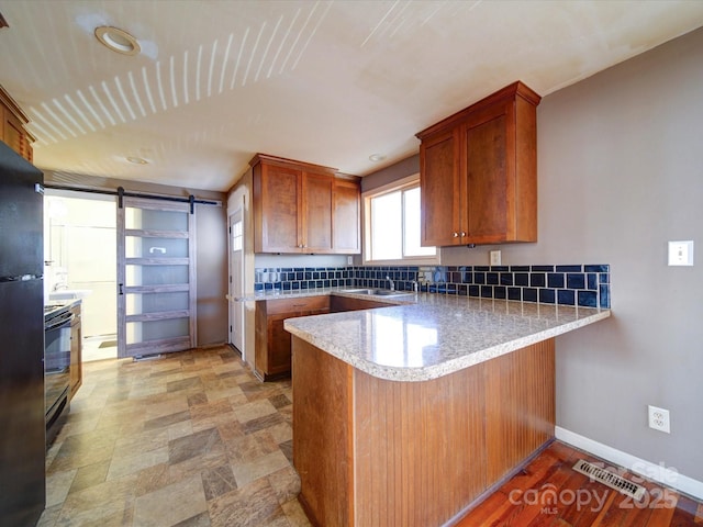 kitchen with a barn door, sink, black electric range oven, and kitchen peninsula