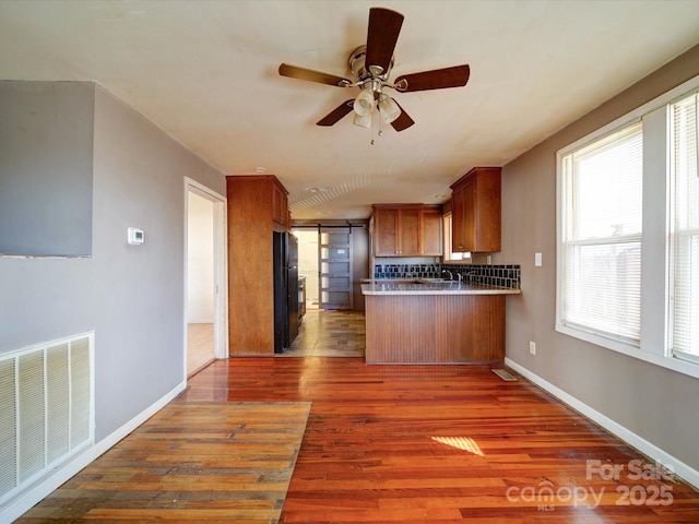 kitchen featuring dark hardwood / wood-style flooring, black fridge, ceiling fan, kitchen peninsula, and a barn door