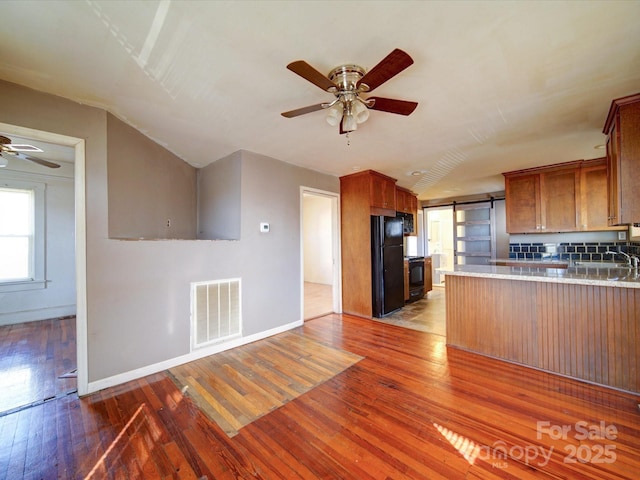 kitchen featuring black refrigerator, dark hardwood / wood-style floors, kitchen peninsula, ceiling fan, and a barn door