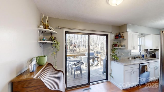 kitchen featuring sink, white cabinetry, light stone counters, light wood-type flooring, and stainless steel dishwasher