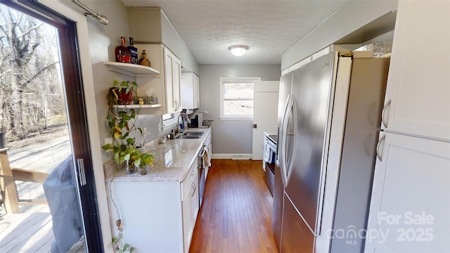 kitchen featuring white cabinetry, wood-type flooring, sink, stainless steel fridge, and light stone countertops