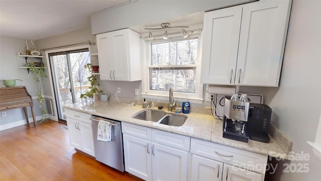 kitchen featuring white cabinetry, sink, stainless steel dishwasher, and light stone countertops