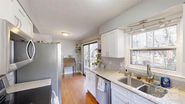 kitchen with white cabinetry, stainless steel appliances, light stone countertops, and sink