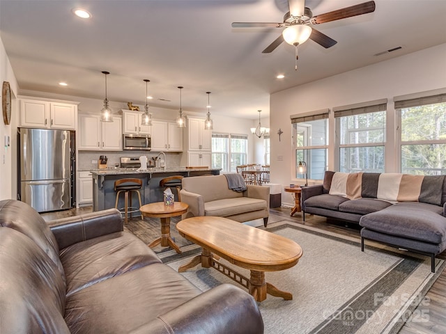 living room with ceiling fan with notable chandelier, sink, and light hardwood / wood-style flooring