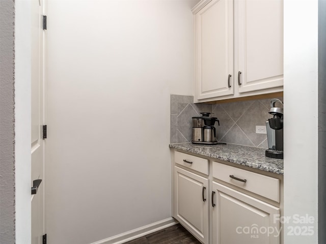 bar with backsplash, dark wood-type flooring, light stone countertops, and white cabinets