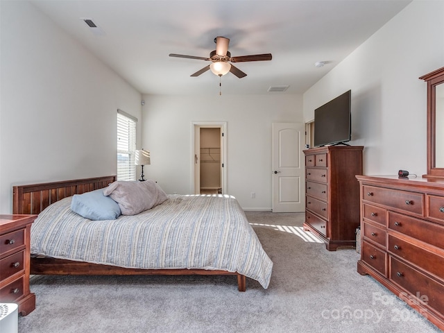 bedroom with ceiling fan, a walk in closet, and light carpet