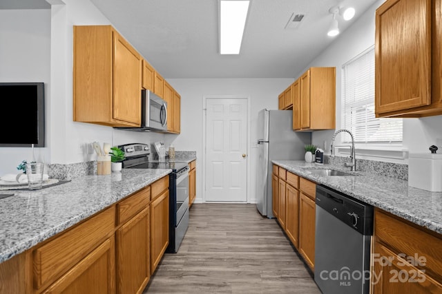 kitchen featuring sink, a textured ceiling, light wood-type flooring, appliances with stainless steel finishes, and light stone countertops