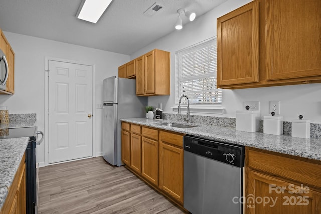 kitchen with sink, light hardwood / wood-style flooring, stainless steel appliances, light stone countertops, and a textured ceiling