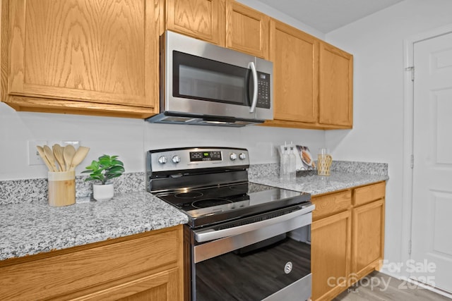 kitchen featuring stainless steel appliances, light brown cabinetry, and light stone countertops