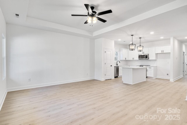 unfurnished living room featuring a tray ceiling, light hardwood / wood-style floors, and ceiling fan