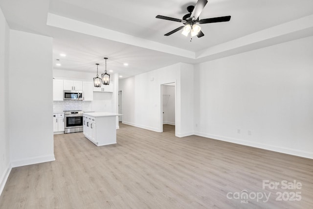 unfurnished living room with a raised ceiling, ceiling fan with notable chandelier, and light hardwood / wood-style flooring