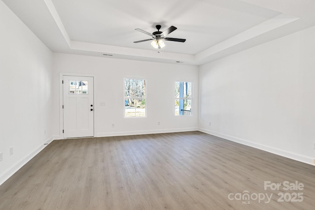 empty room with a raised ceiling, a wealth of natural light, and light wood-type flooring