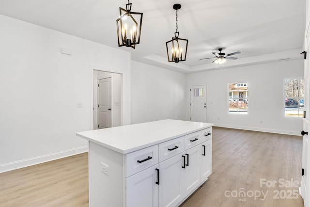 kitchen with light hardwood / wood-style flooring, white cabinetry, hanging light fixtures, a center island, and a tray ceiling