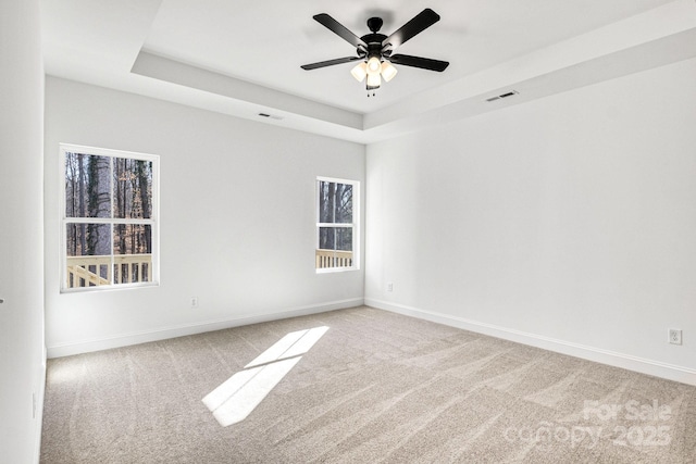 carpeted spare room featuring a tray ceiling and ceiling fan