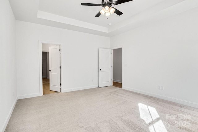 unfurnished bedroom with ceiling fan, a tray ceiling, and light colored carpet