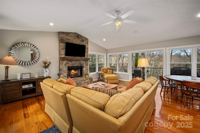 living room featuring ceiling fan, lofted ceiling, a stone fireplace, and light hardwood / wood-style floors