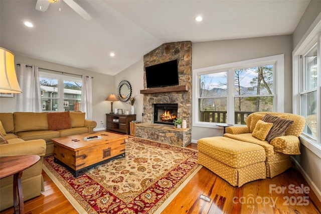 living room with hardwood / wood-style flooring, a stone fireplace, and vaulted ceiling