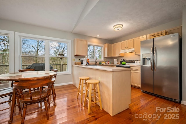 kitchen with a kitchen bar, sink, light wood-type flooring, kitchen peninsula, and stainless steel appliances