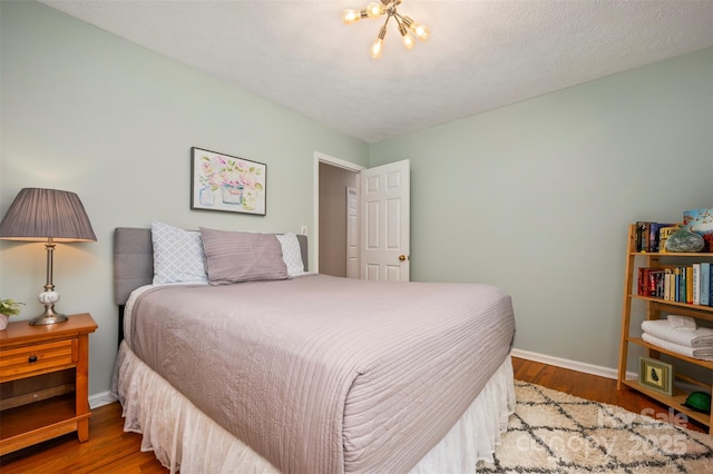 bedroom with hardwood / wood-style flooring, an inviting chandelier, and a textured ceiling