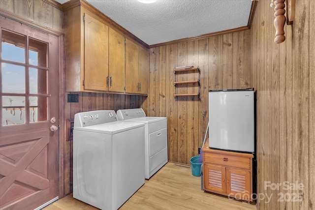 laundry area with cabinets, separate washer and dryer, a textured ceiling, light wood-type flooring, and wooden walls